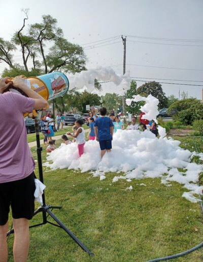Summer reading 2025 kick-off party kids playing outside the library with foam.