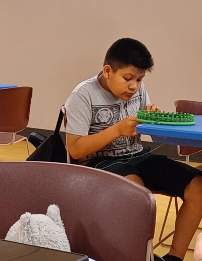 Boy working in loom knitting during a craft program at tht library
